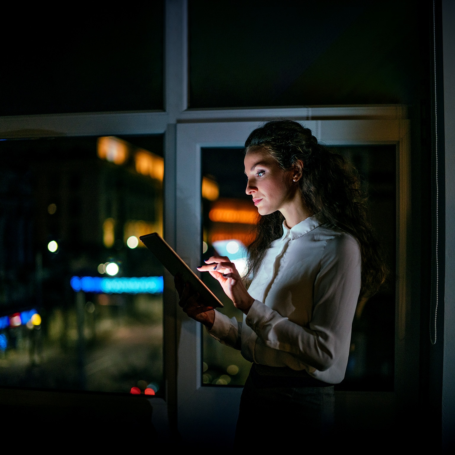 Image of a businesswoman working late on a digital tablet in an office.