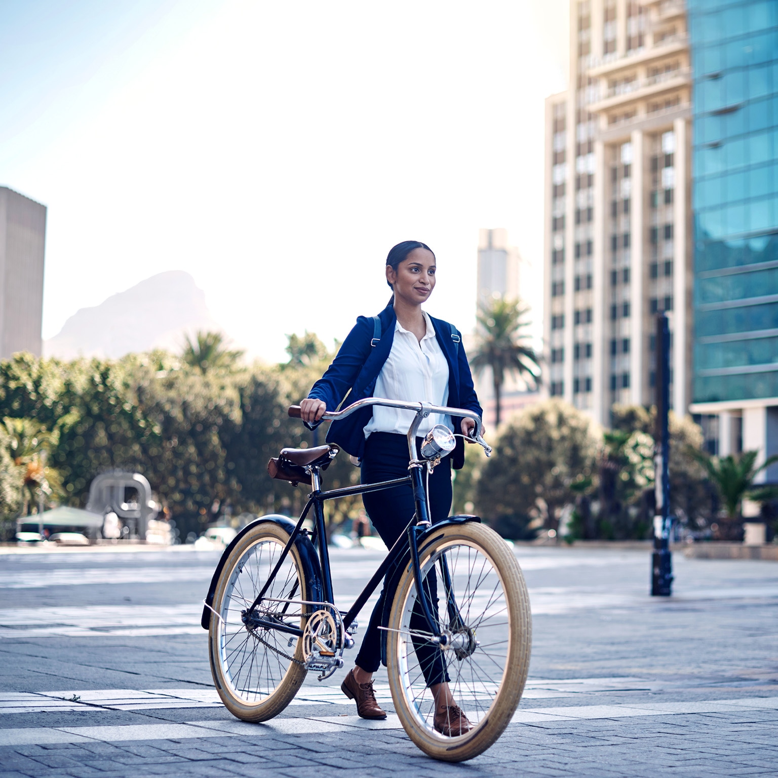  A young South African businesswoman walking her bicycle through a modern downtown. Table mountain is seen in the distance. 