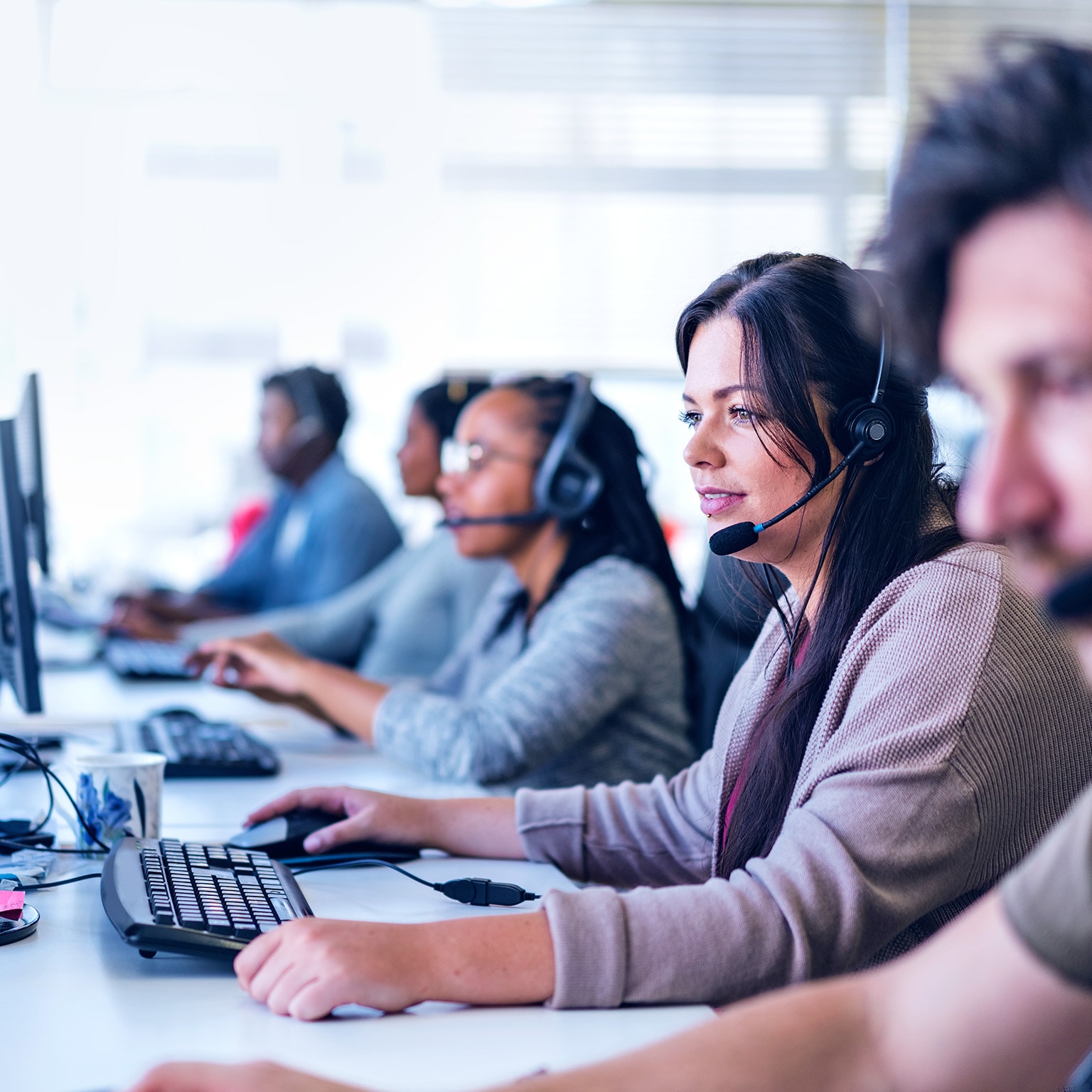 Young businesswoman wearing headset while using computer. Row of operators are sitting at desk. They are working in call center. - stock photo