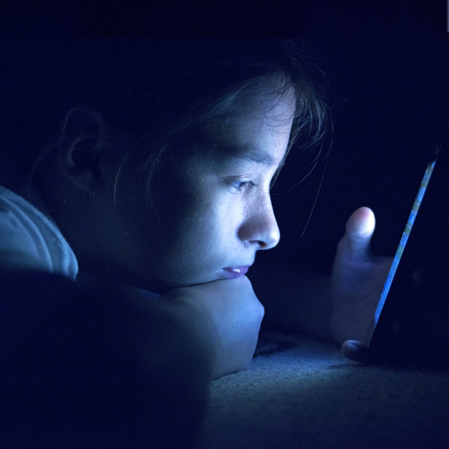 Child staring at phone in a dark room