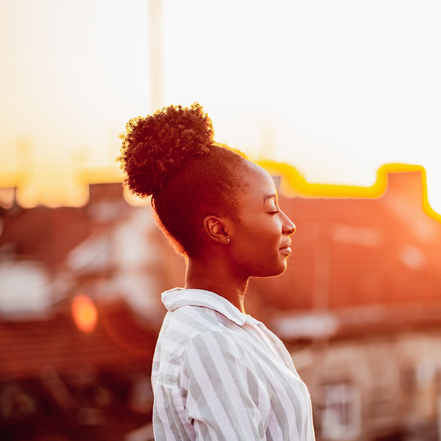 Young African American woman is relaxing on the rooftop with sunset light on her face